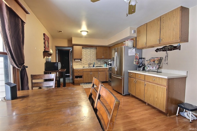 kitchen with ceiling fan, sink, stainless steel appliances, light hardwood / wood-style floors, and decorative backsplash