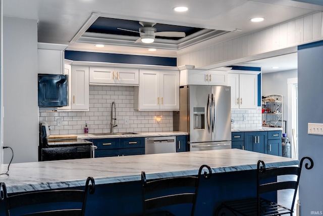 kitchen with a breakfast bar, sink, blue cabinetry, white cabinetry, and stainless steel appliances