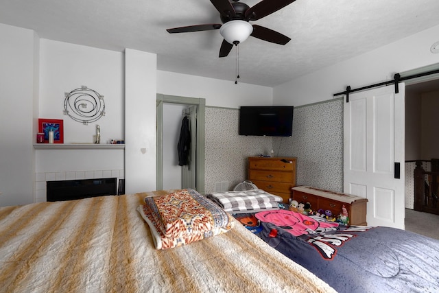 bedroom featuring a barn door, ceiling fan, a closet, and a tile fireplace