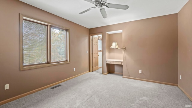 unfurnished bedroom featuring light carpet, built in desk, and ceiling fan