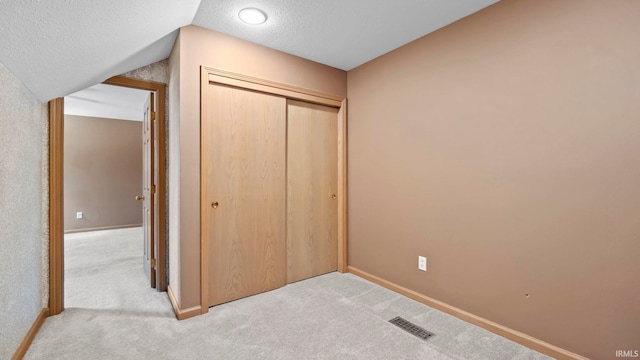 unfurnished bedroom with lofted ceiling, a closet, carpet, and a textured ceiling