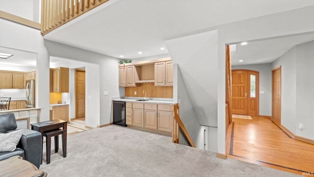 kitchen featuring sink, black dishwasher, light brown cabinetry, light colored carpet, and stainless steel refrigerator