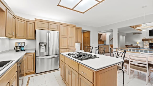 kitchen with a center island, a stone fireplace, decorative light fixtures, light tile patterned flooring, and stainless steel appliances