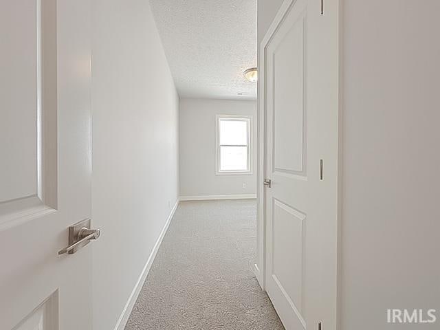 hall with light colored carpet and a textured ceiling