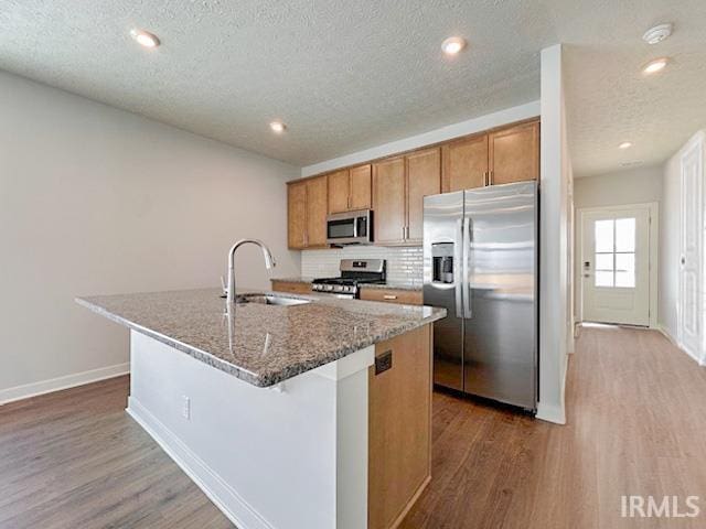 kitchen featuring sink, stainless steel appliances, an island with sink, dark stone counters, and a textured ceiling