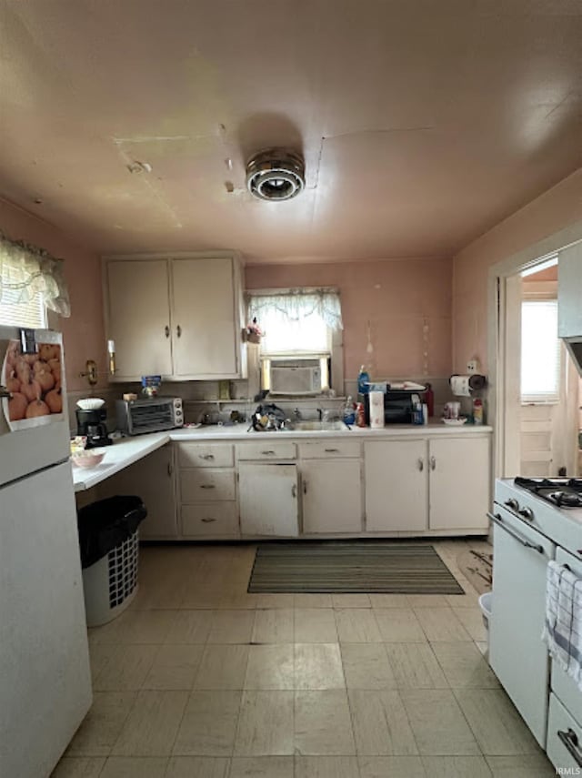 kitchen featuring white appliances, white cabinetry, and a wealth of natural light