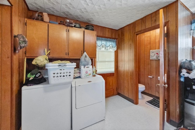 clothes washing area featuring cabinets, washing machine and dryer, and wood walls