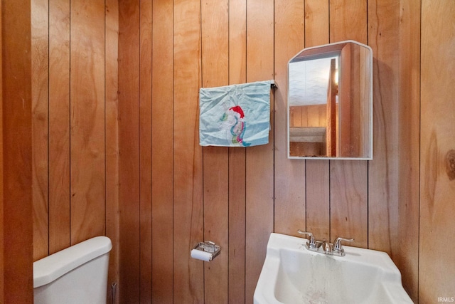 bathroom with wood walls, toilet, and sink