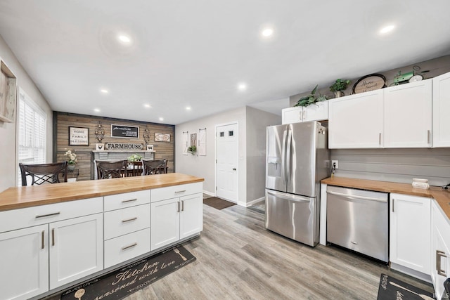 kitchen with butcher block counters, wood walls, white cabinets, and appliances with stainless steel finishes