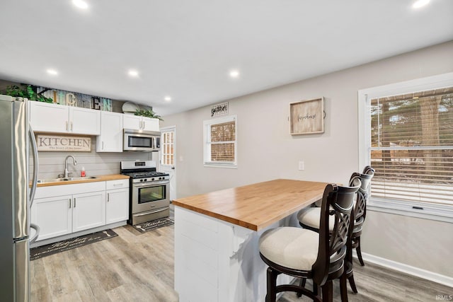 kitchen with butcher block countertops, white cabinets, a kitchen bar, and appliances with stainless steel finishes