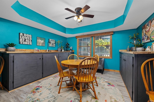 dining room with ceiling fan, light hardwood / wood-style floors, a raised ceiling, and wet bar