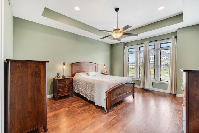 bedroom with ceiling fan, dark wood-type flooring, and a tray ceiling