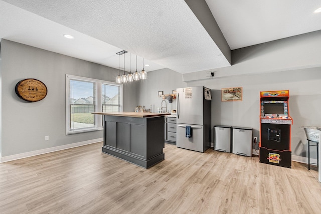 kitchen with hanging light fixtures, light wood-type flooring, a textured ceiling, a kitchen island, and stainless steel refrigerator