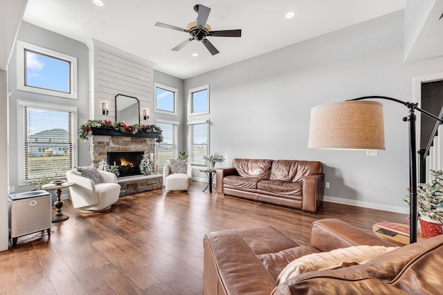 living room with ceiling fan, wood-type flooring, a fireplace, and a towering ceiling