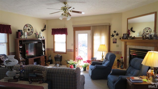 living room featuring a tiled fireplace, ceiling fan, carpet floors, and a textured ceiling