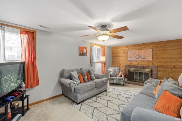 living room featuring ceiling fan, wood walls, light colored carpet, and a brick fireplace