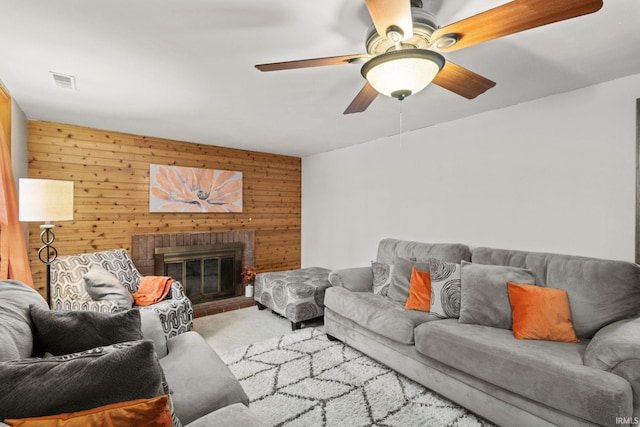 carpeted living room featuring a brick fireplace, ceiling fan, and wooden walls