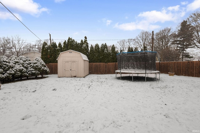 snowy yard featuring a storage shed and a trampoline