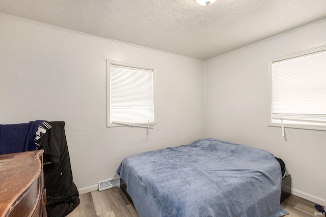 bedroom featuring crown molding, light wood-type flooring, a textured ceiling, and multiple windows