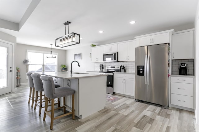 kitchen featuring stainless steel appliances, sink, pendant lighting, white cabinets, and an island with sink