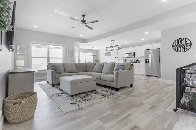 living room featuring light hardwood / wood-style flooring, ceiling fan with notable chandelier, and sink