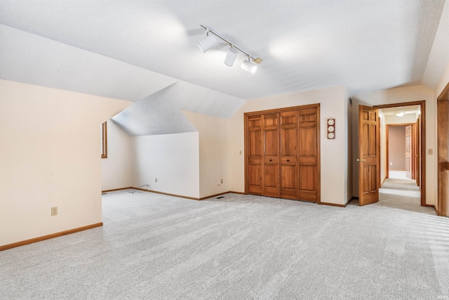 additional living space with a textured ceiling, light carpet, and vaulted ceiling