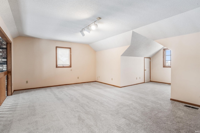 additional living space featuring a textured ceiling, light carpet, and lofted ceiling