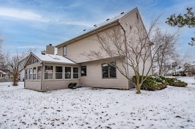 snow covered back of property with a sunroom