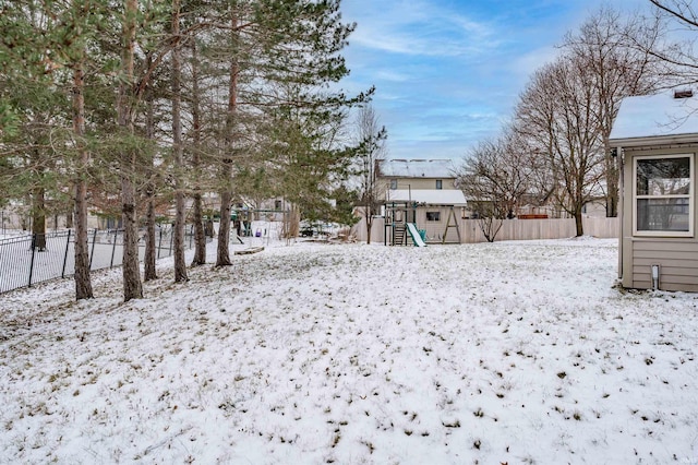 yard layered in snow featuring a shed and a playground