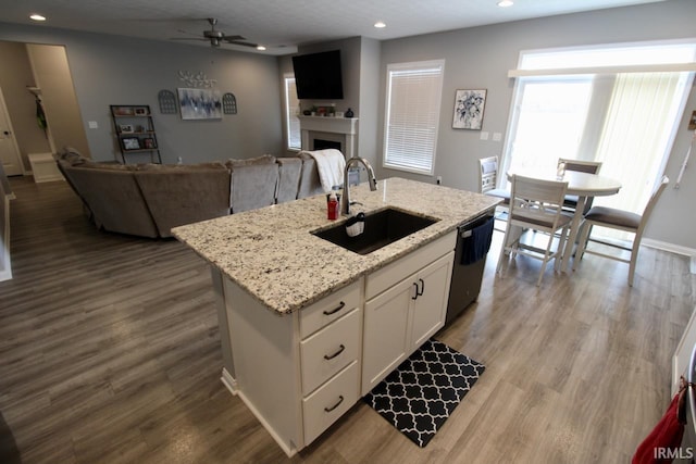 kitchen with light stone countertops, sink, black dishwasher, white cabinetry, and an island with sink