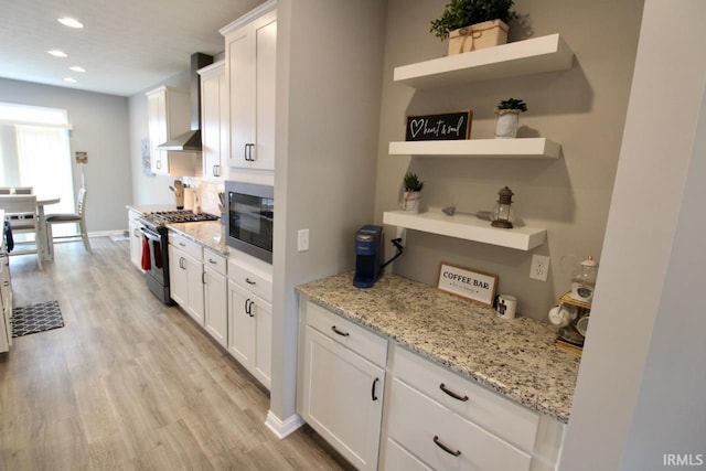 kitchen with gas stove, built in microwave, white cabinetry, light stone countertops, and wall chimney range hood