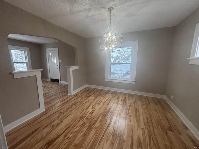 unfurnished dining area with wood-type flooring, a textured ceiling, and a chandelier