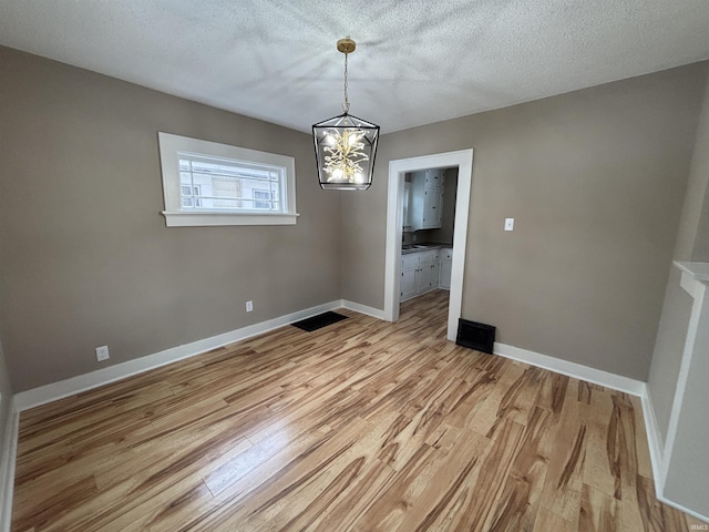 unfurnished dining area with a textured ceiling, light hardwood / wood-style flooring, and a chandelier