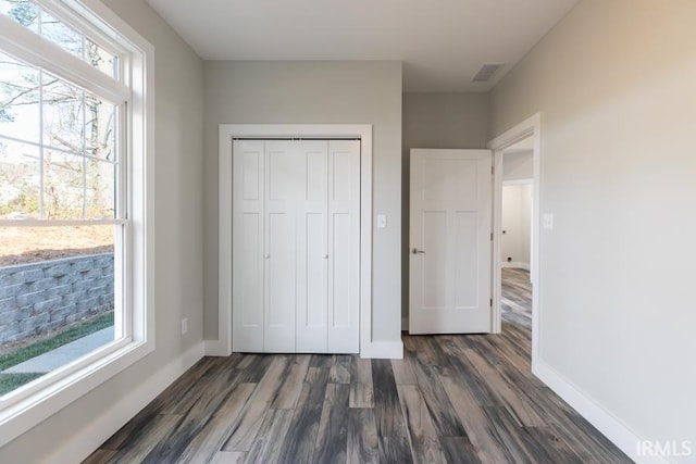 unfurnished bedroom with dark hardwood / wood-style floors, multiple windows, and a closet