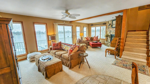 carpeted living room featuring ceiling fan, a healthy amount of sunlight, a water view, and a fireplace