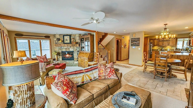 living room featuring ceiling fan with notable chandelier, beam ceiling, a stone fireplace, and a wealth of natural light