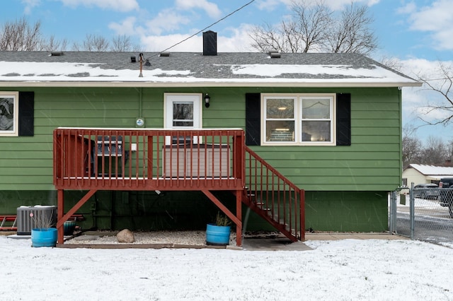 snow covered back of property with a deck and central AC unit