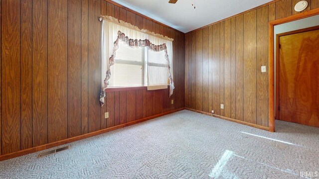 spare room with ceiling fan, wood walls, and light carpet