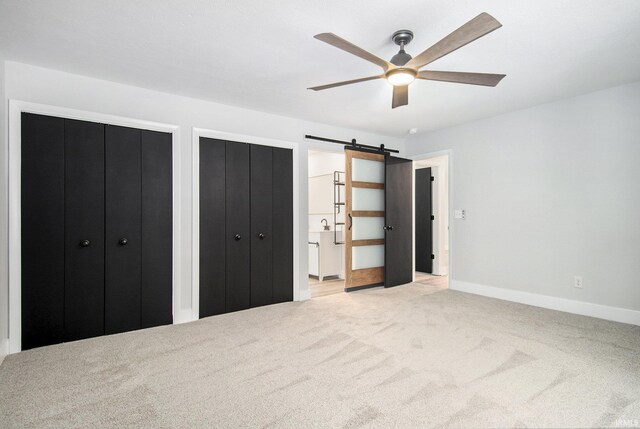 unfurnished bedroom with light carpet, a barn door, two closets, and ceiling fan