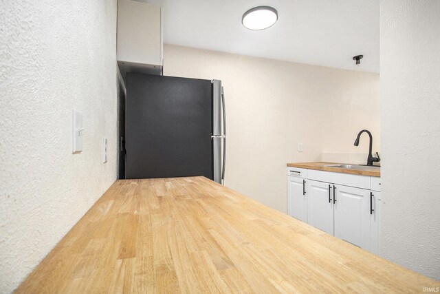 kitchen featuring sink, light hardwood / wood-style flooring, stainless steel fridge, white cabinetry, and butcher block counters