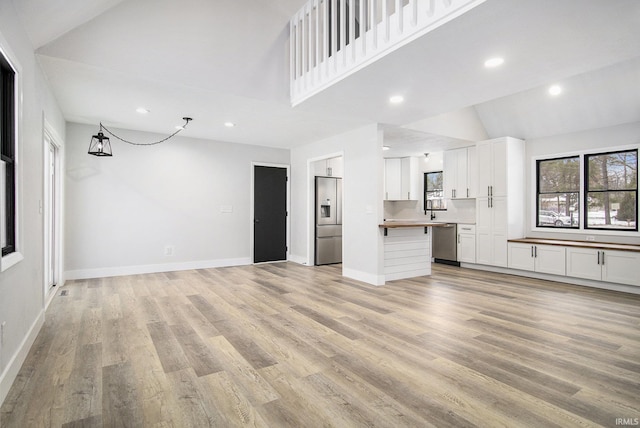 unfurnished living room featuring an inviting chandelier, sink, high vaulted ceiling, and light hardwood / wood-style flooring