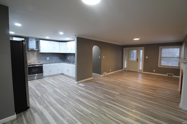 kitchen featuring wall chimney exhaust hood, black fridge, backsplash, electric stove, and white cabinets