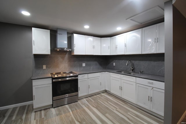 kitchen featuring white cabinets, sink, wall chimney exhaust hood, light hardwood / wood-style floors, and stainless steel range oven