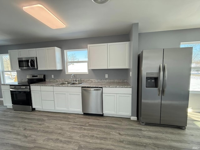 kitchen with light wood-type flooring, light stone counters, stainless steel appliances, sink, and white cabinetry