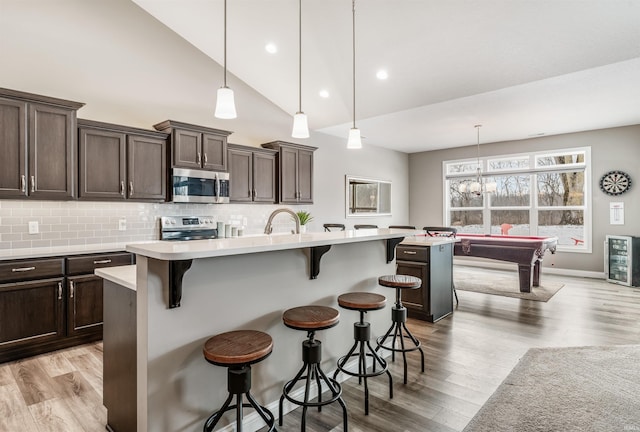 kitchen with appliances with stainless steel finishes, tasteful backsplash, a breakfast bar, a center island with sink, and pool table