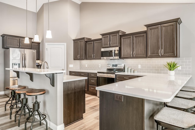 kitchen featuring high vaulted ceiling, hanging light fixtures, light wood-type flooring, appliances with stainless steel finishes, and a kitchen bar