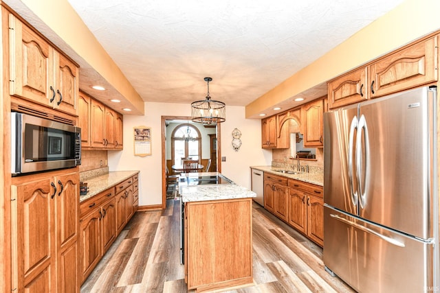 kitchen featuring stainless steel appliances, pendant lighting, a center island with sink, a notable chandelier, and light hardwood / wood-style floors