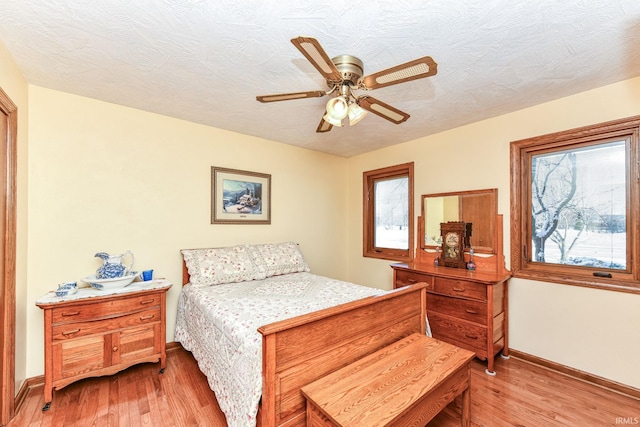 bedroom with ceiling fan, light hardwood / wood-style floors, and a textured ceiling