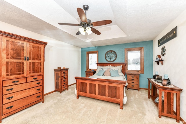 bedroom featuring a raised ceiling, ceiling fan, light colored carpet, and a textured ceiling