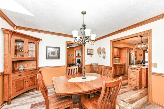 dining space with light hardwood / wood-style flooring, ornamental molding, and an inviting chandelier